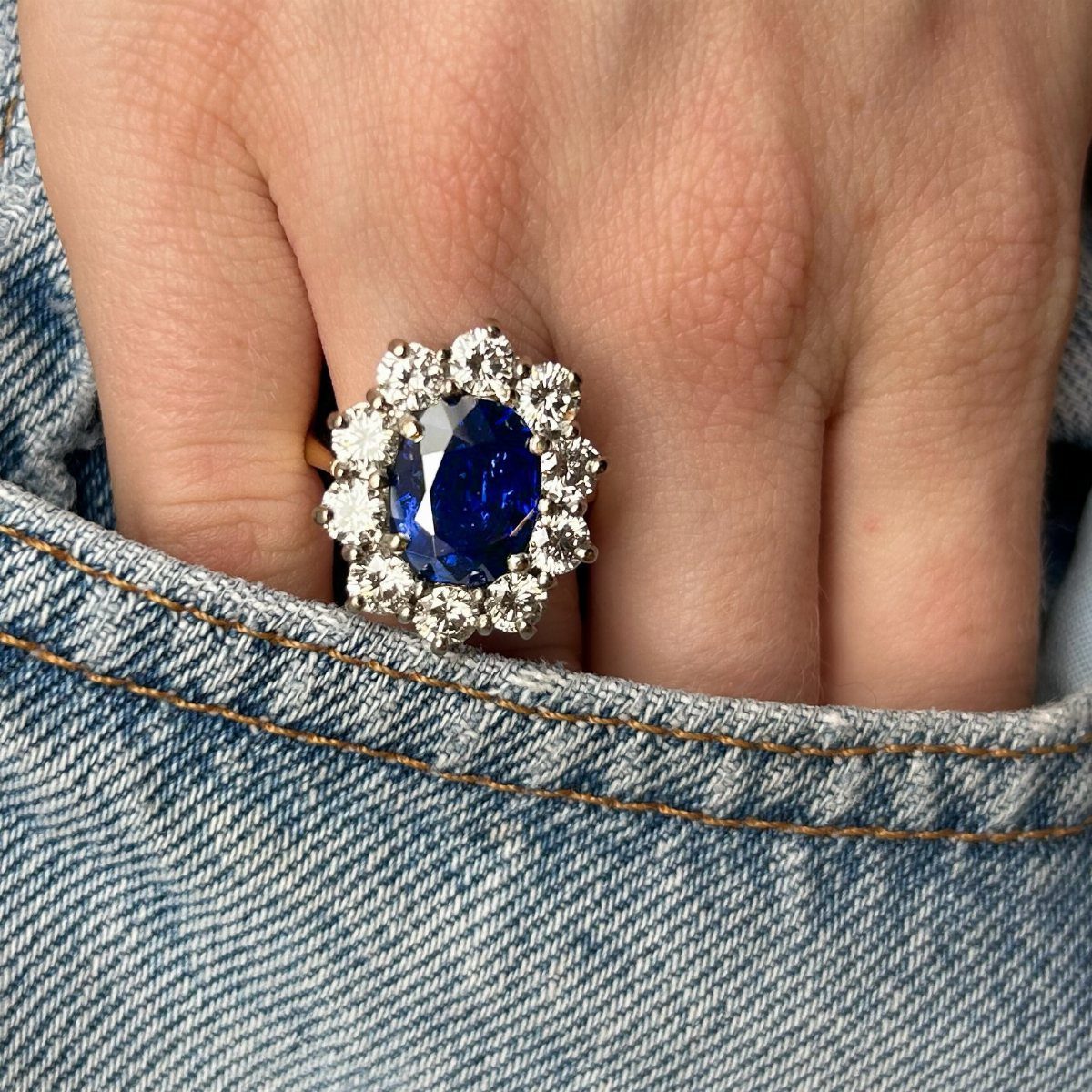 Sapphire and diamond ring on a finger resting against blue denim fabric