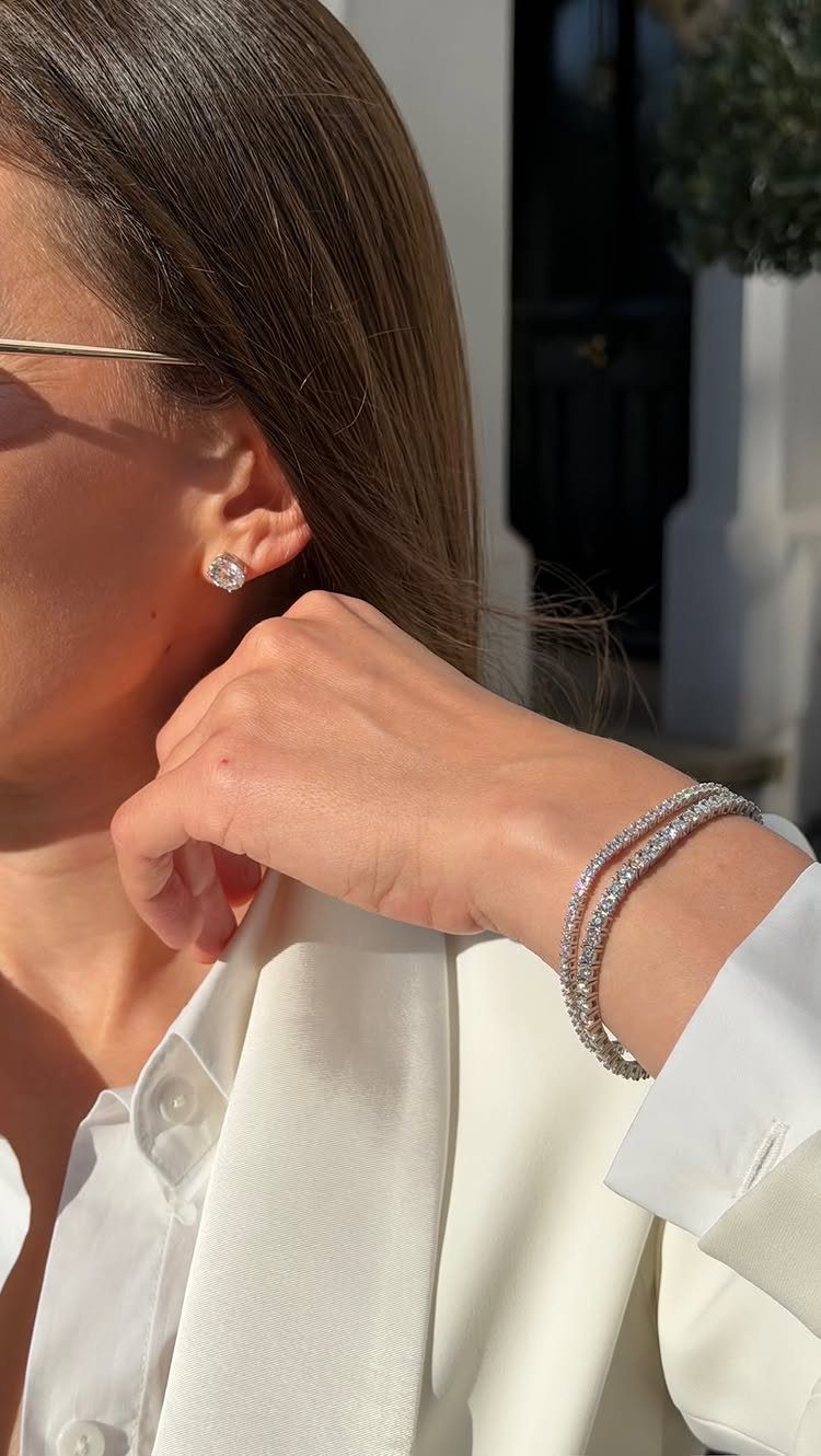Woman wearing diamond stud earrings and two diamond tennis bracelets with white blazer