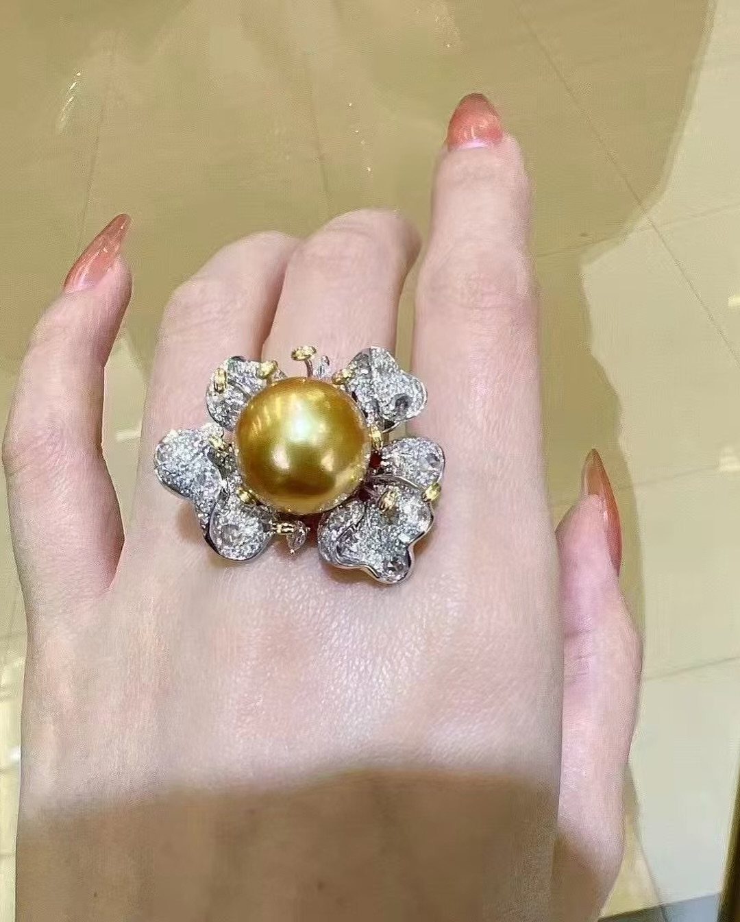 Gold ring with a large golden pearl and diamond floral accents on a finger
