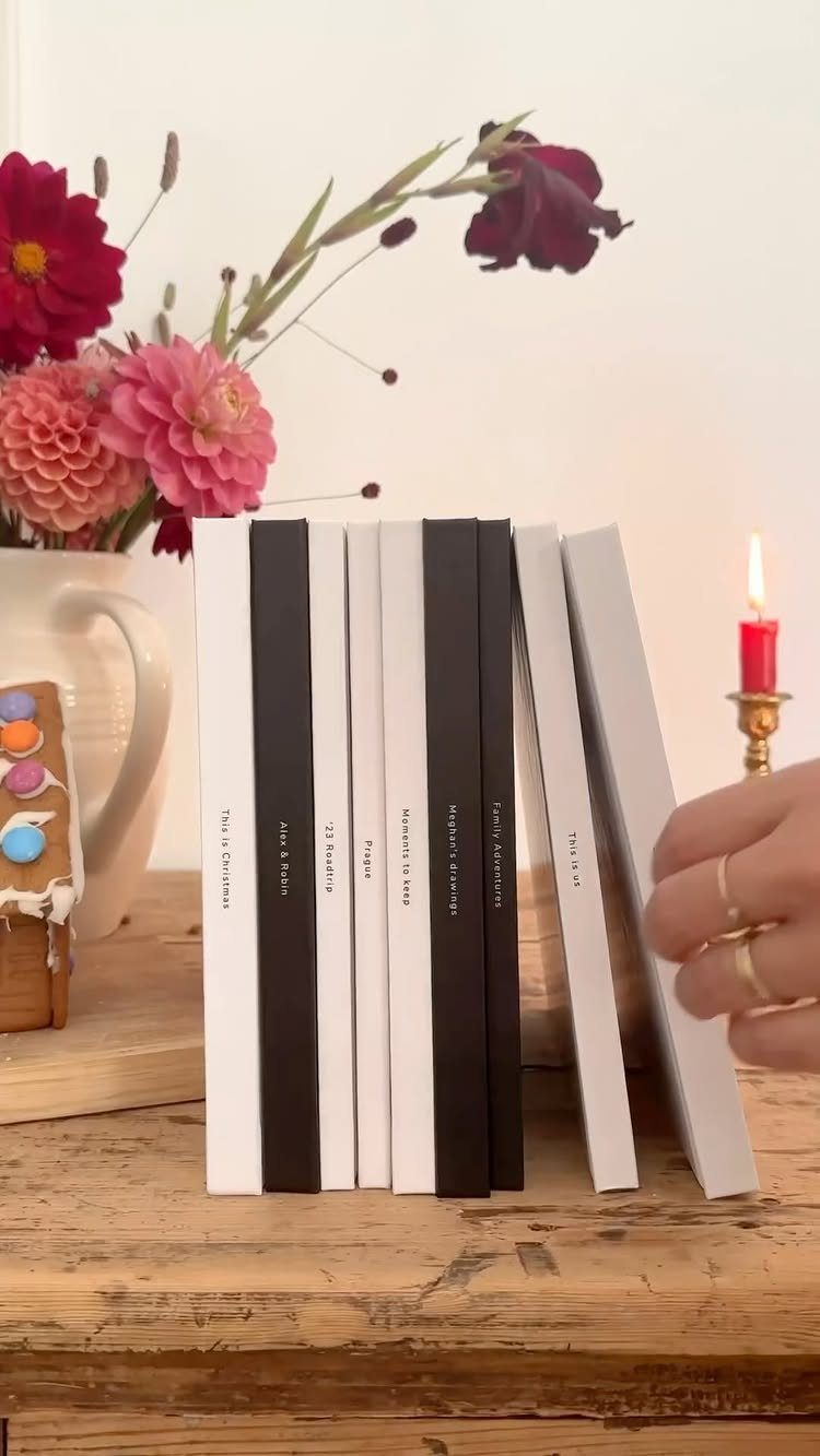 White and black hardcover photo books on a wooden table with flowers and candle.