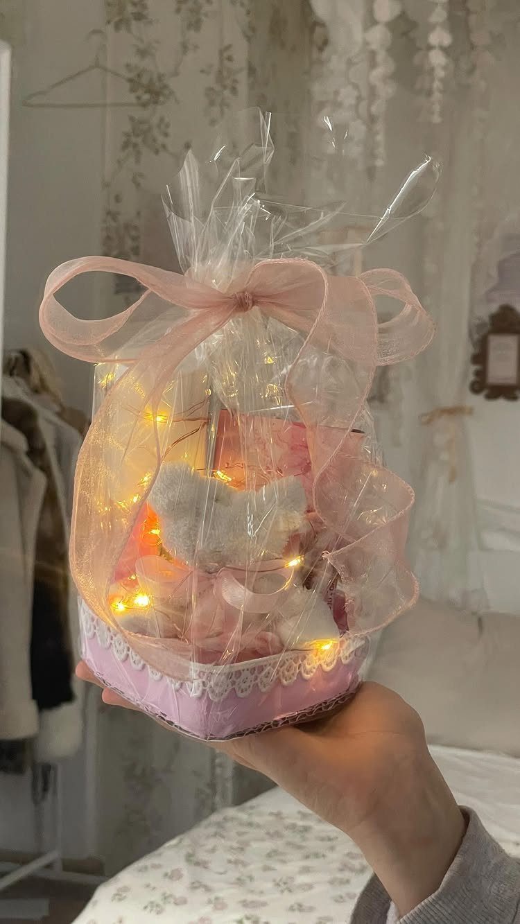 Pink gift basket wrapped in cellophane with fairy lights and plush toys.
