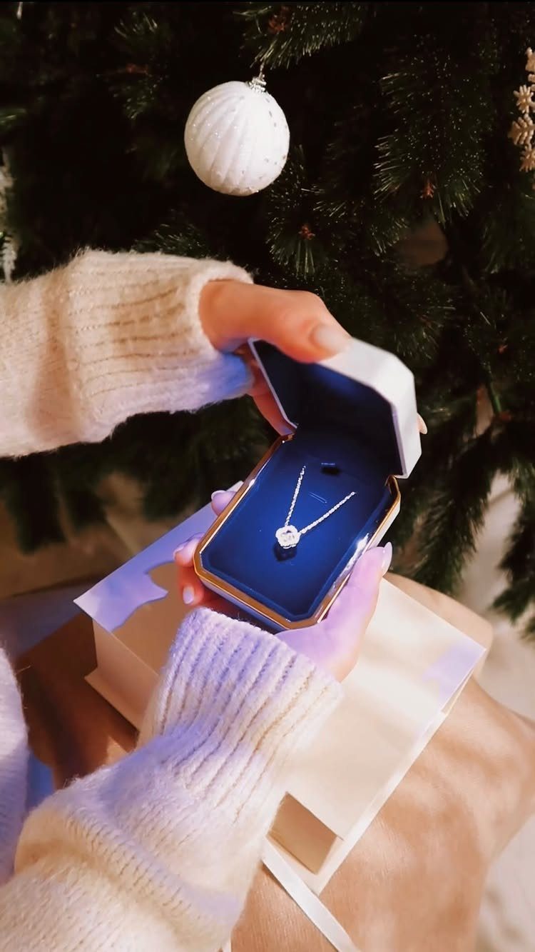 Silver diamond necklace in a blue box held in front of a Christmas tree