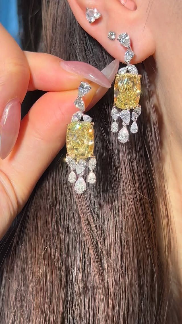 Yellow gemstone and diamond earrings worn and held by a woman