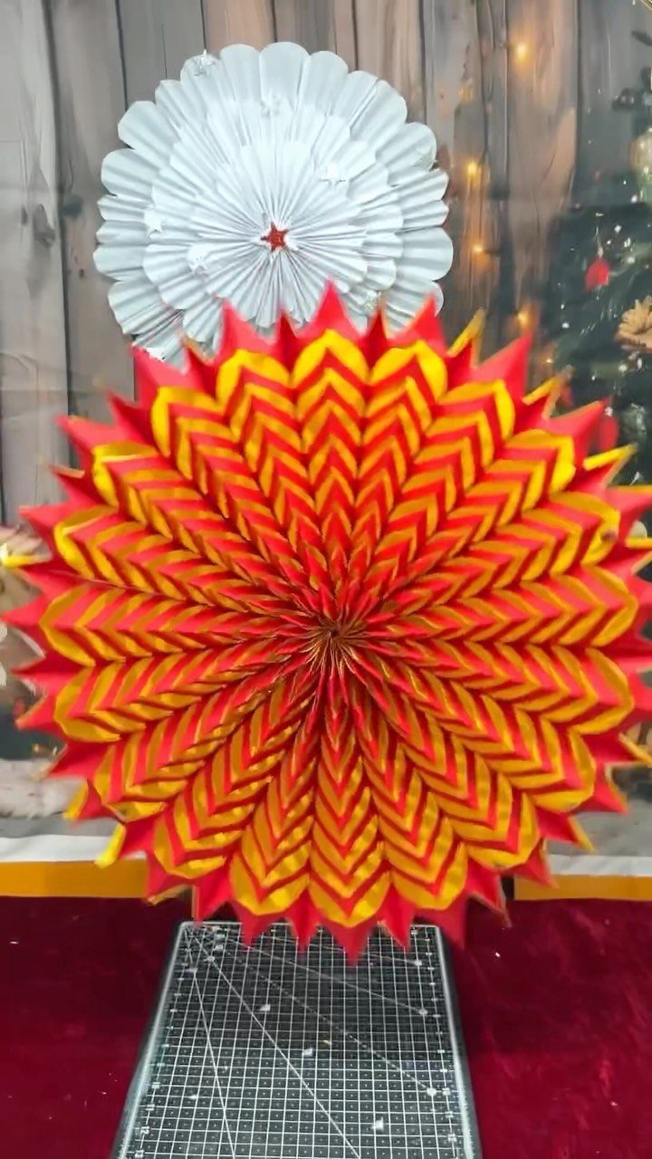 Red and yellow 3D paper snowflake ornament with a white one behind it.