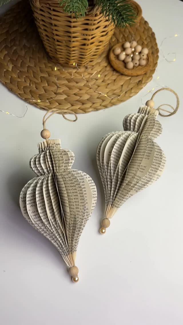 Two folded book page ornaments with wooden beads on a white surface.