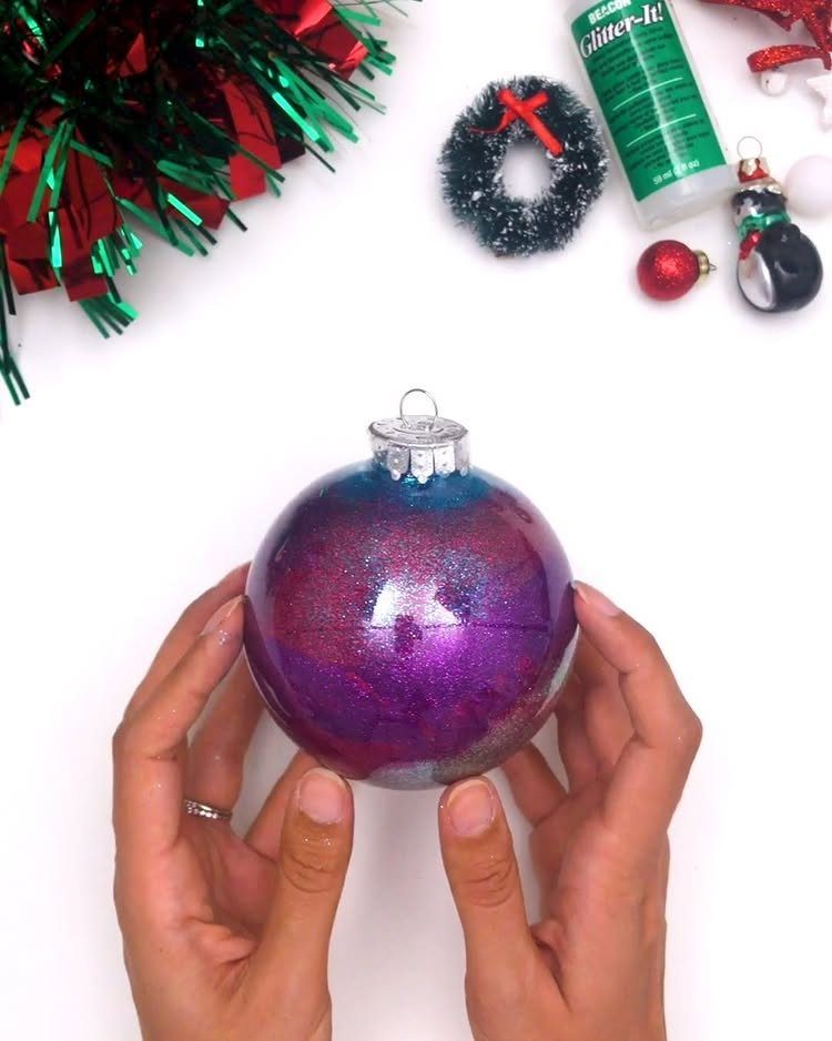Hands holding a clear Christmas ornament filled with sparkling purple and pink glitter.