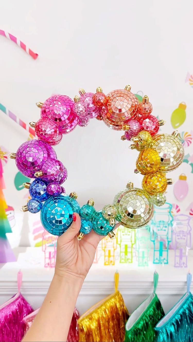 Colorful disco ball ornament wreath held by a hand against a white background.