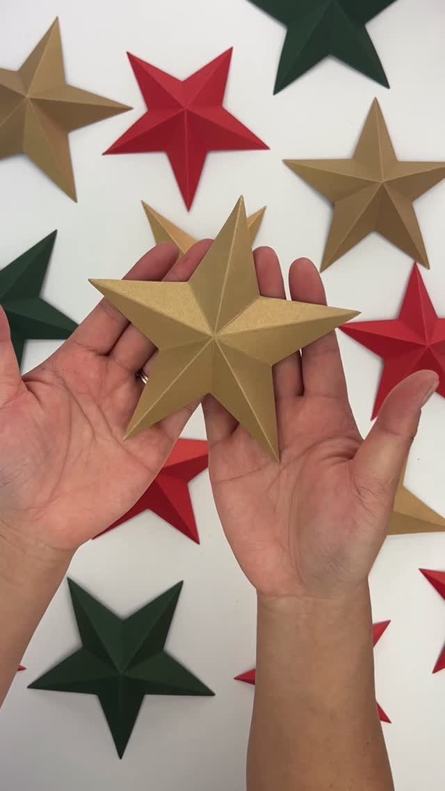 Hands holding a gold 3D paper star surrounded by red and green stars.