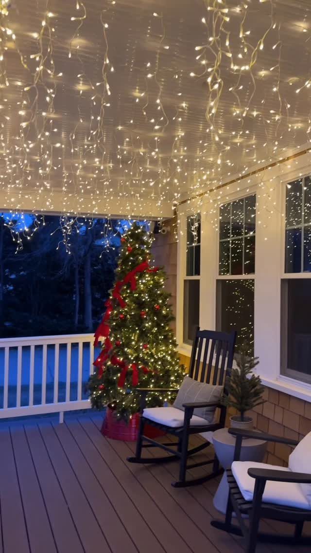 Christmas porch with warm white ceiling lights, a decorated tree, and rocking chairs.