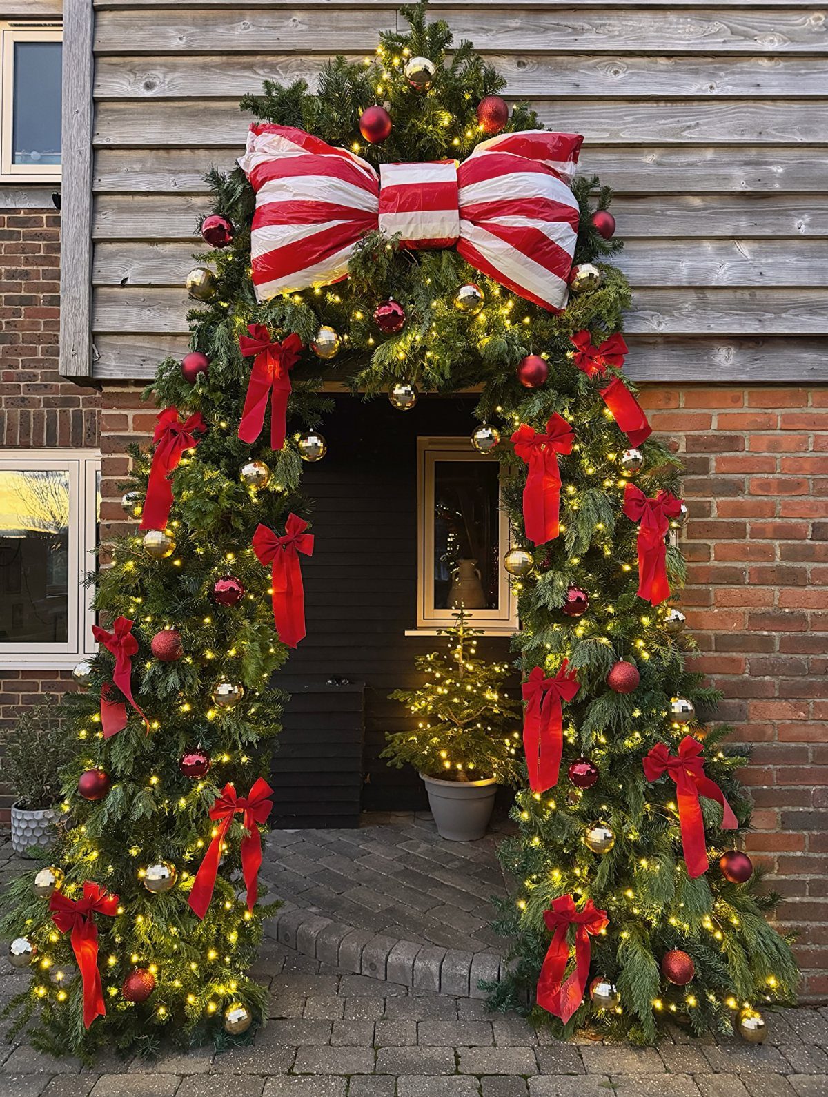 Arched evergreen garland with red bows and lights framing a home entrance