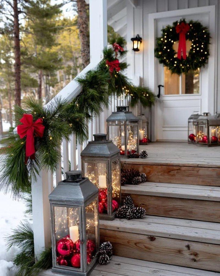 Christmas decorated porch with green garlands, red bows, and lanterns on wooden steps.