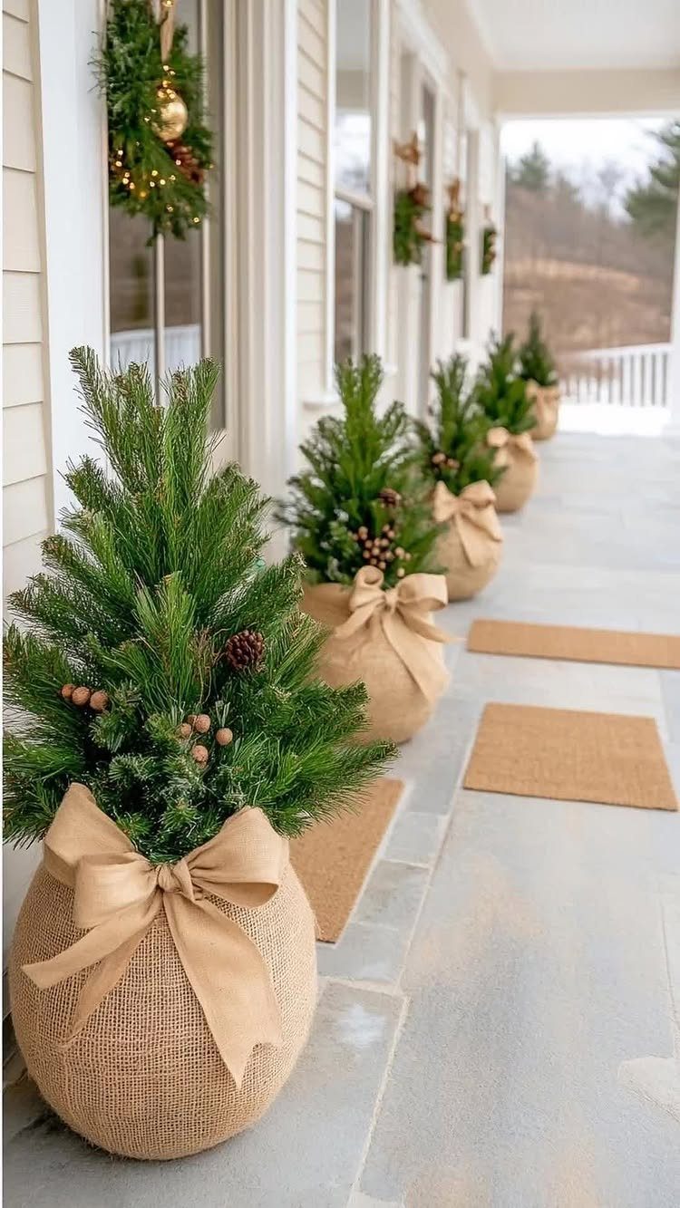 Small evergreen trees in burlap pots with bows lining a white porch