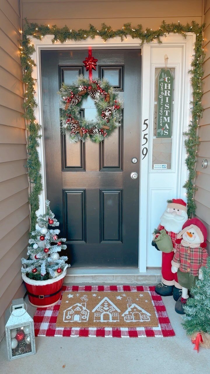Christmas porch decor featuring a black door, red and white accents, and festive figures.