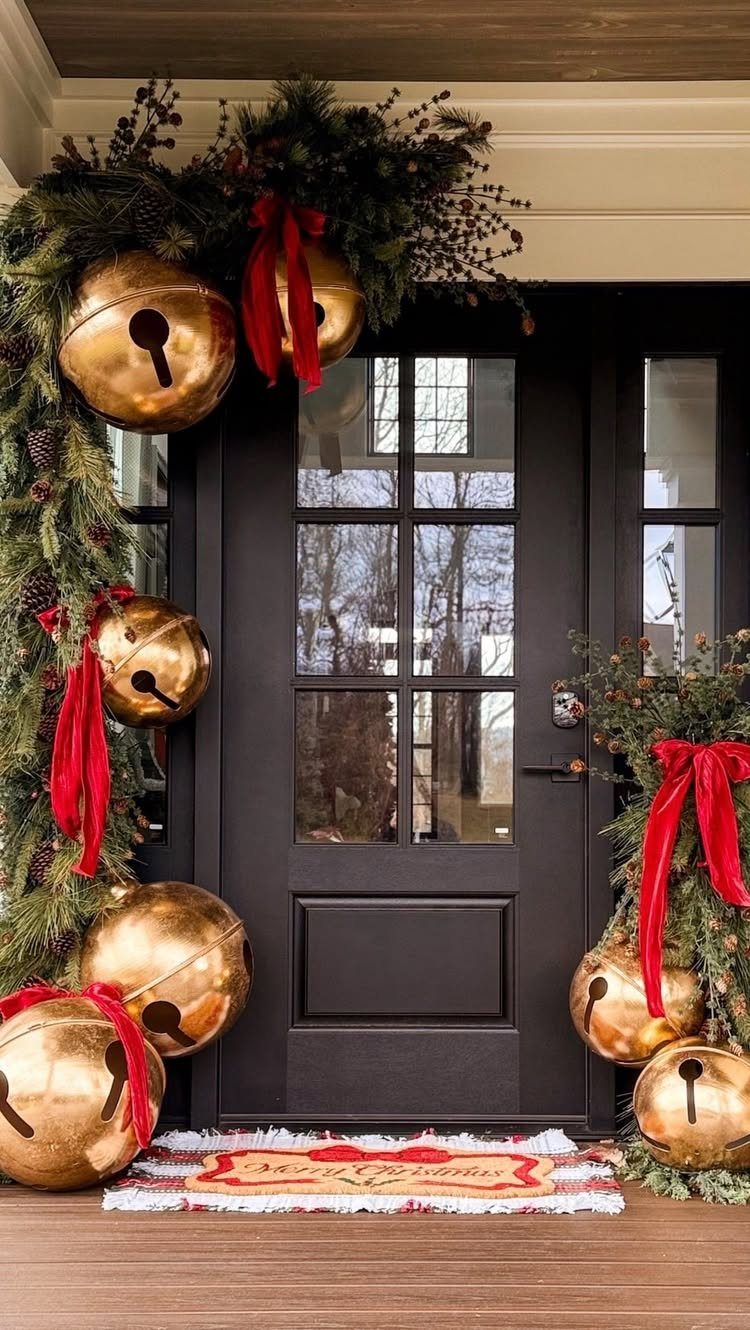 Black front door adorned with green garland, gold bells, and red ribbons.