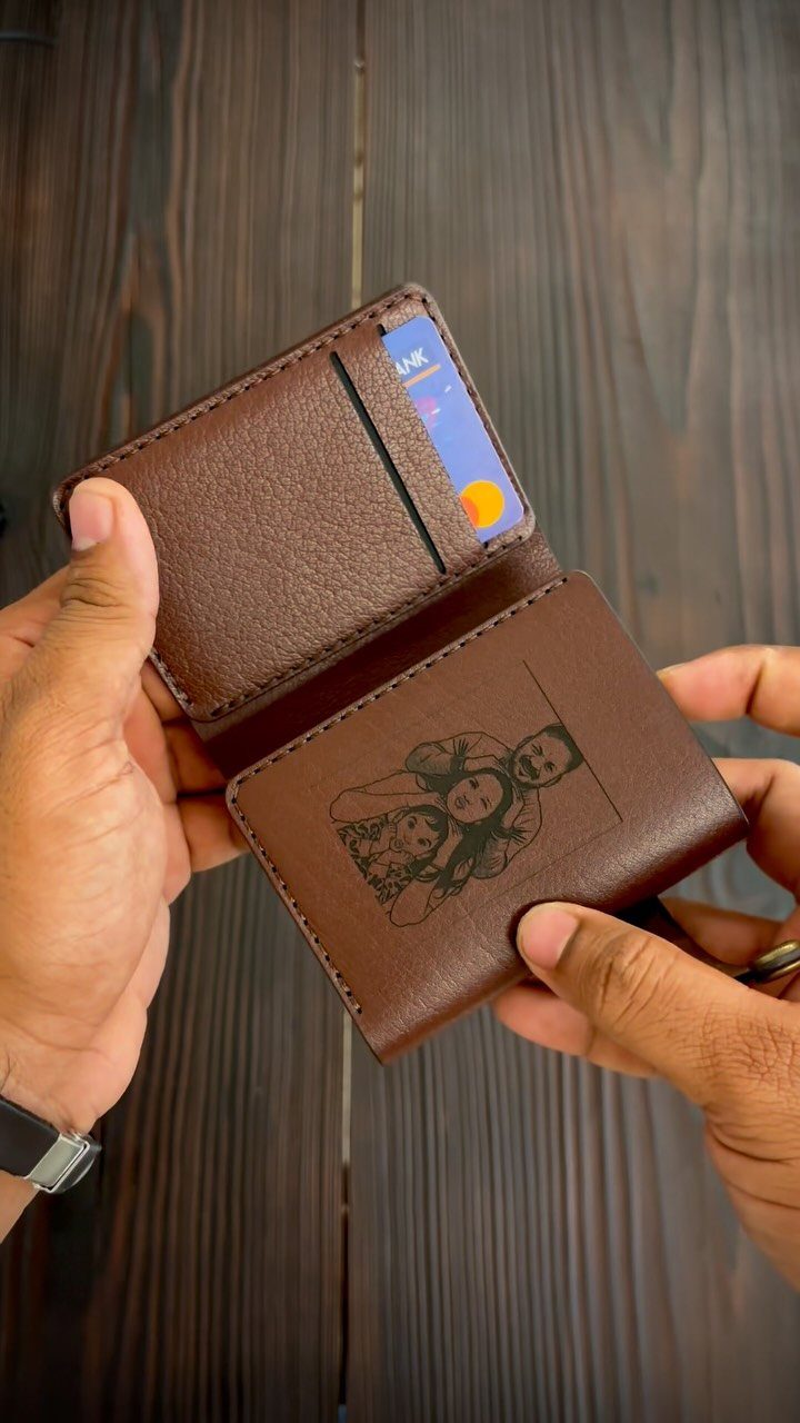 Brown leather wallet held open showing an engraved couple illustration and credit card.