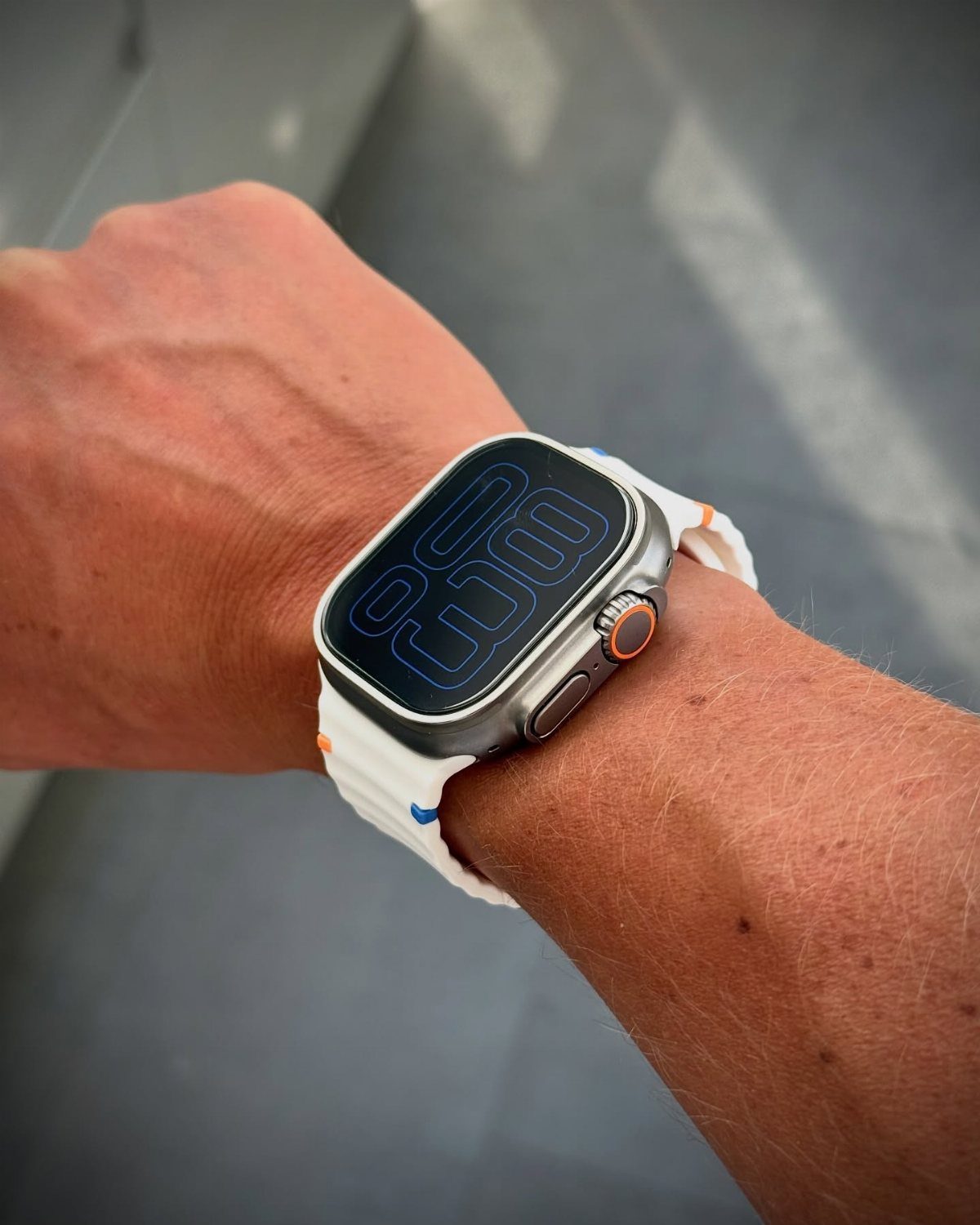 Silver smartwatch with white strap on a man's wrist against grey background