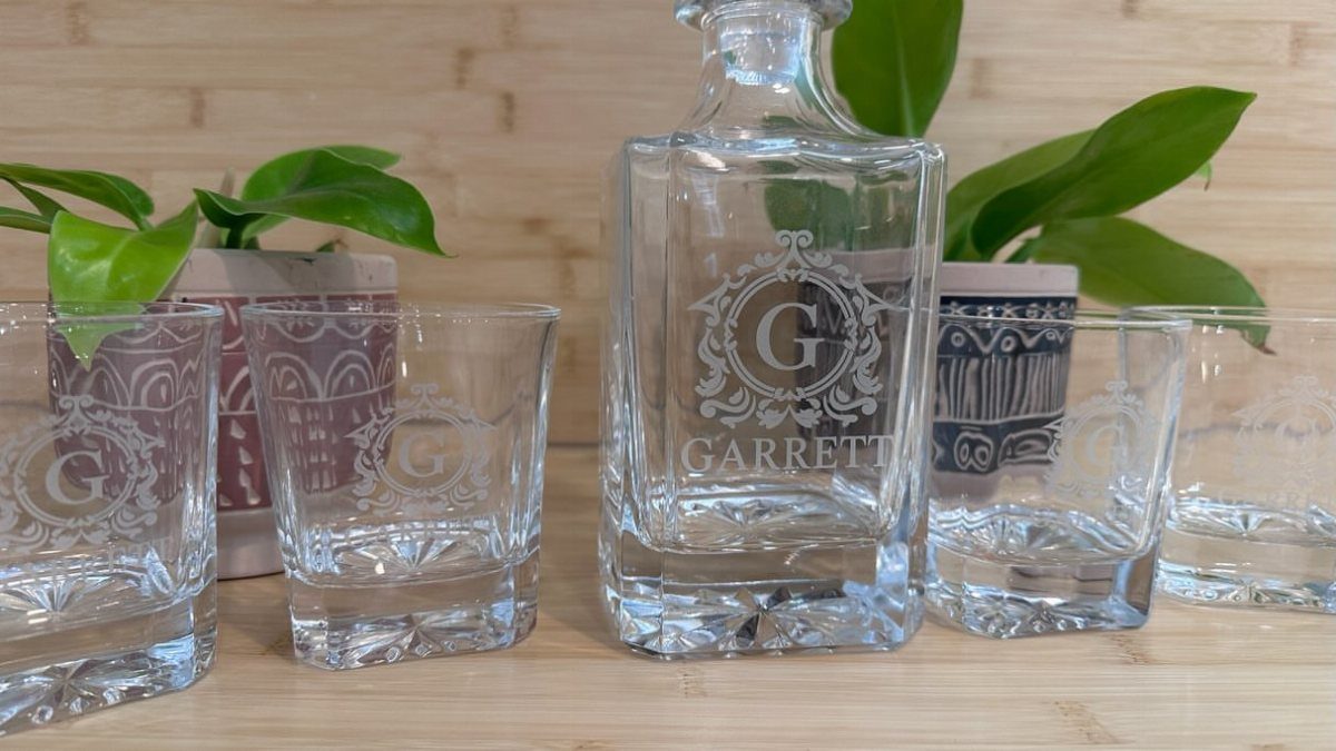 Engraved glass decanter and matching glasses with a monogram and name on wood.