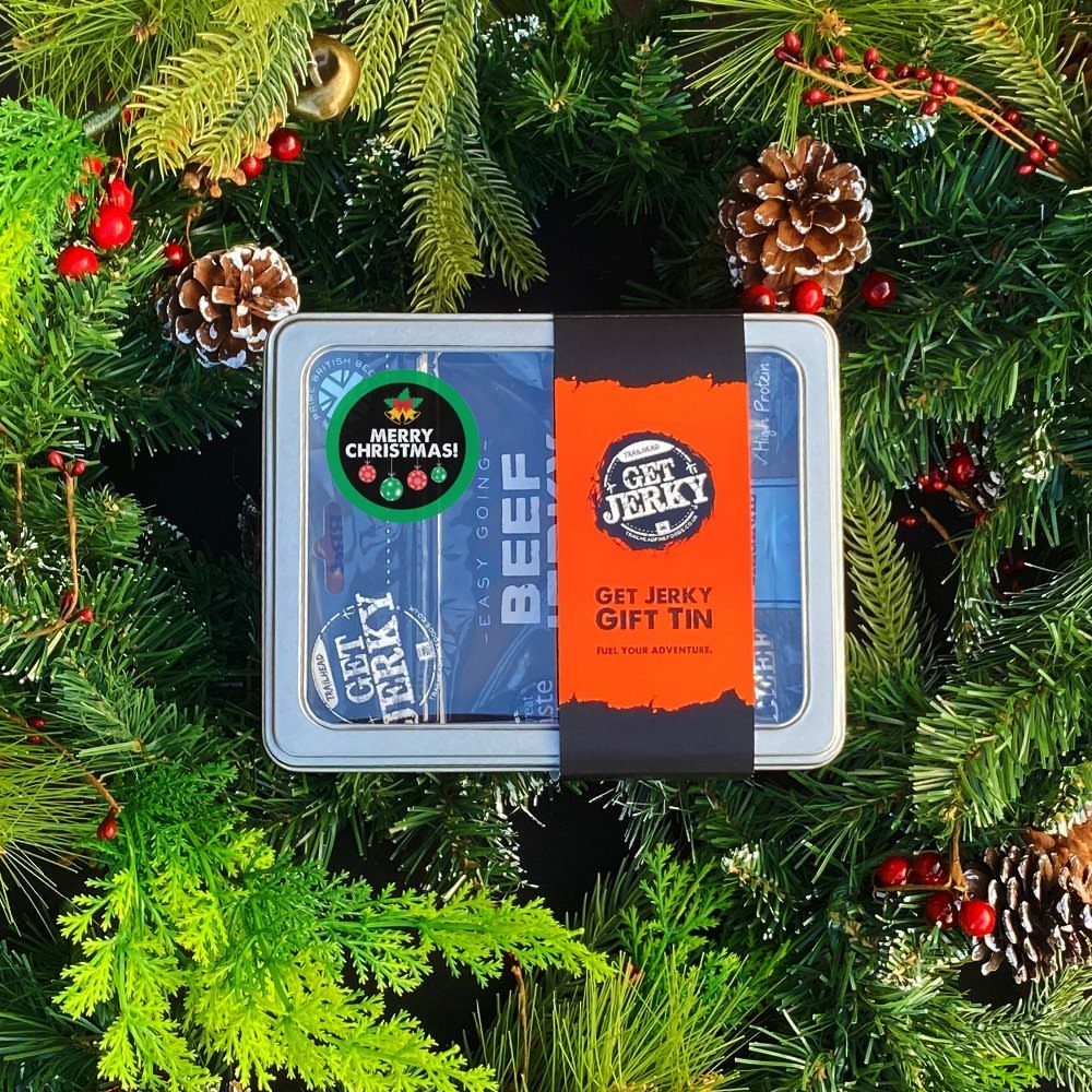 Beef jerky gift tin surrounded by festive green pine branches and red berries.