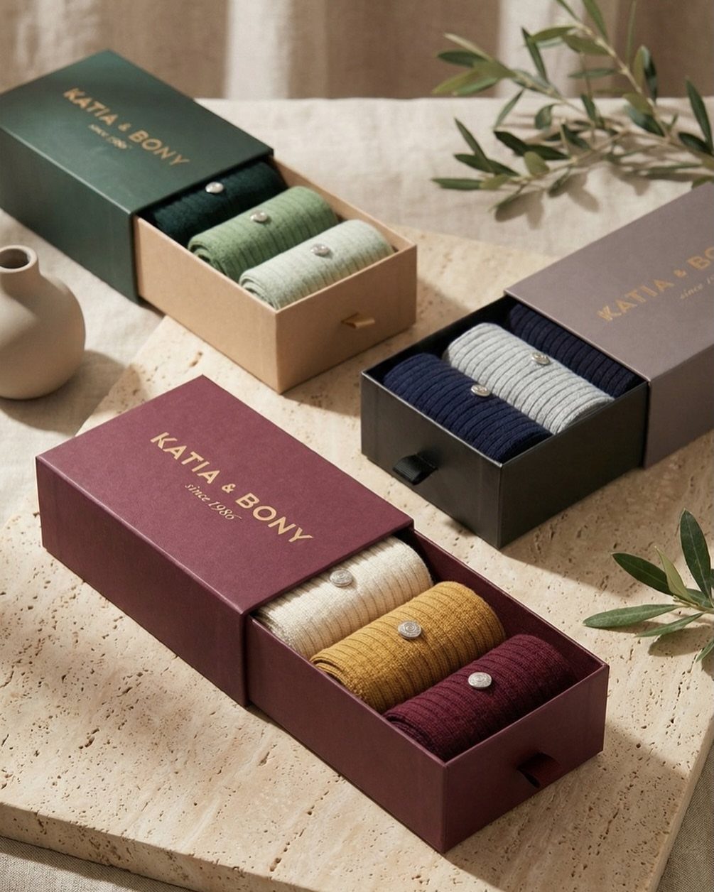 Three gift boxes with rolled colorful socks on a stone surface with olive leaves