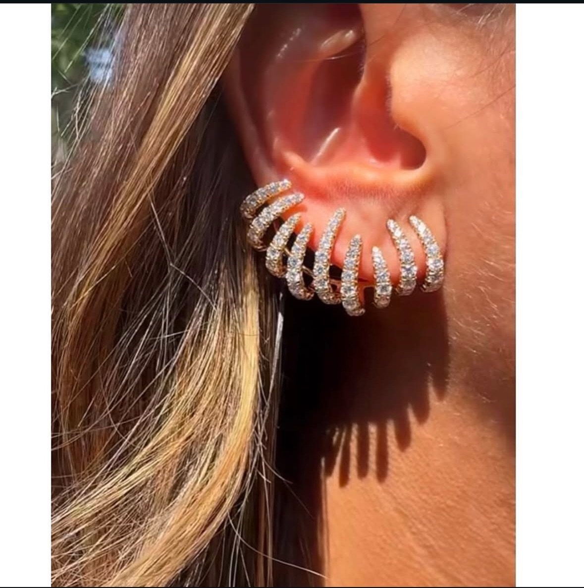 Gold crystal ear cuff worn on a person's ear in bright sunlight.