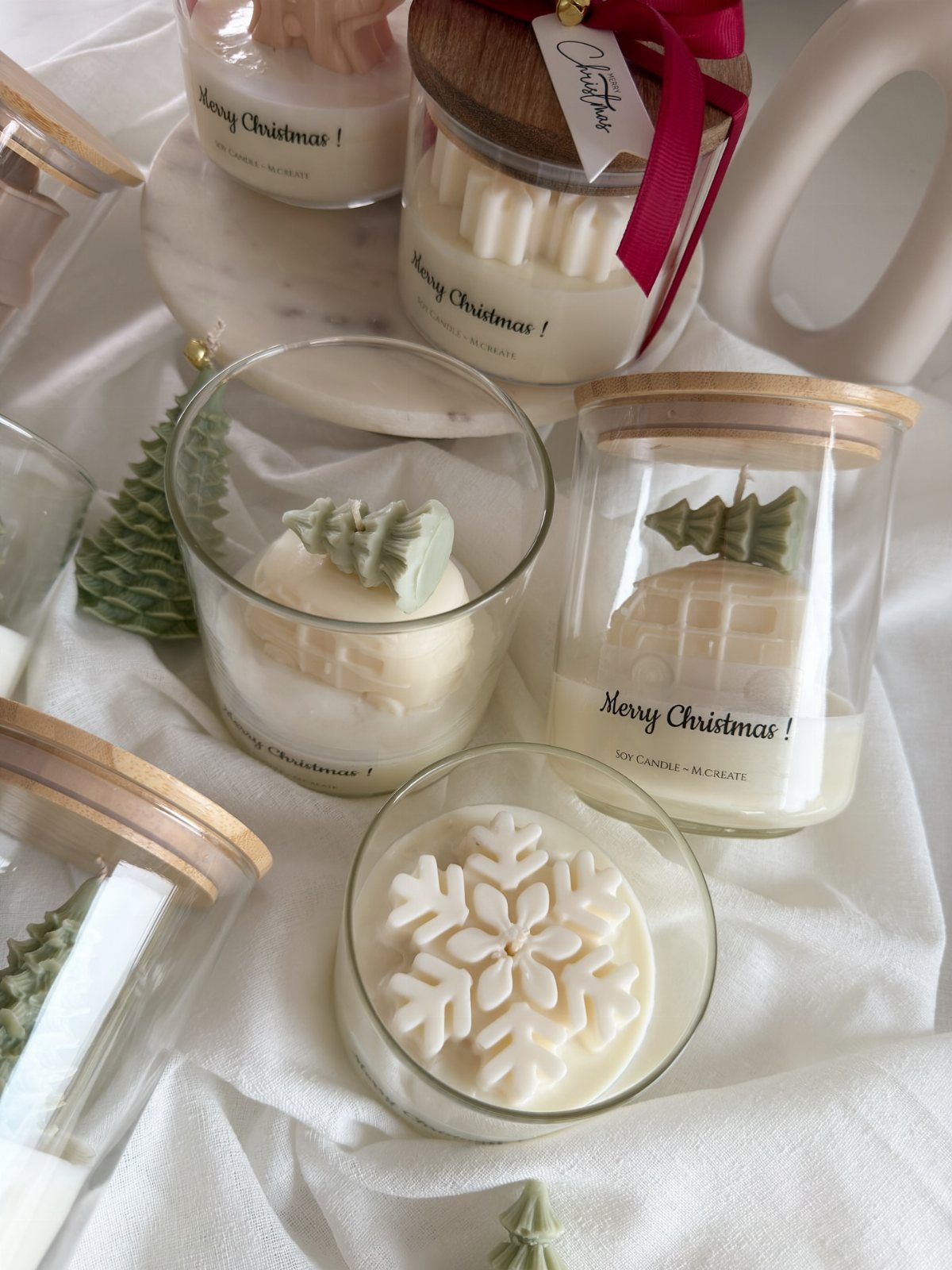 White Christmas candles in glass jars with wax snowflakes and green trees.
