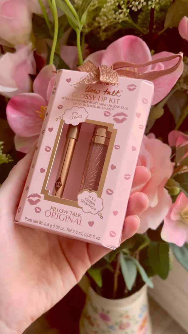 Charlotte Tilbury Pillow Talk Glossy Lip Kit held against a backdrop of pink flowers.