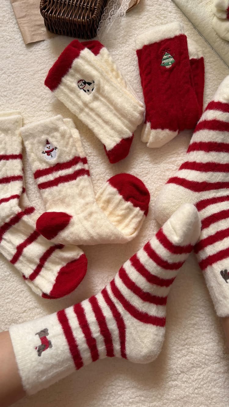 Fuzzy cream and red striped Christmas socks and red mittens on white fabric.