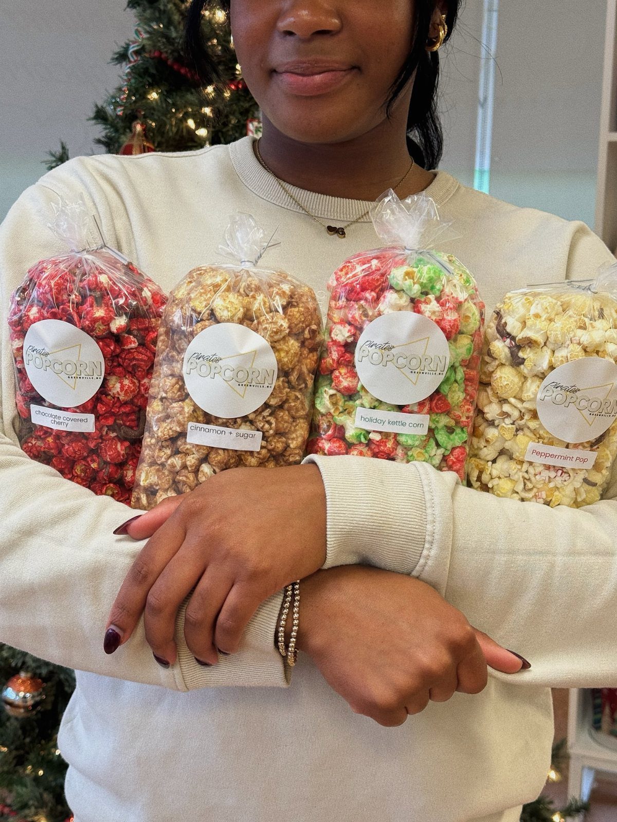 Four bags of colorful gourmet popcorn held by a person in a cream sweater.