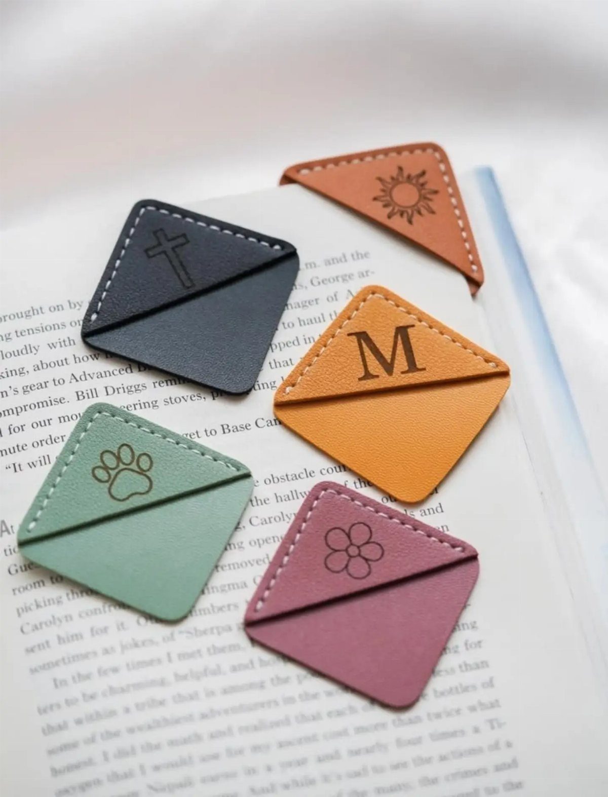 Triangular leather bookmarks with embossed initials and symbols resting on an open book