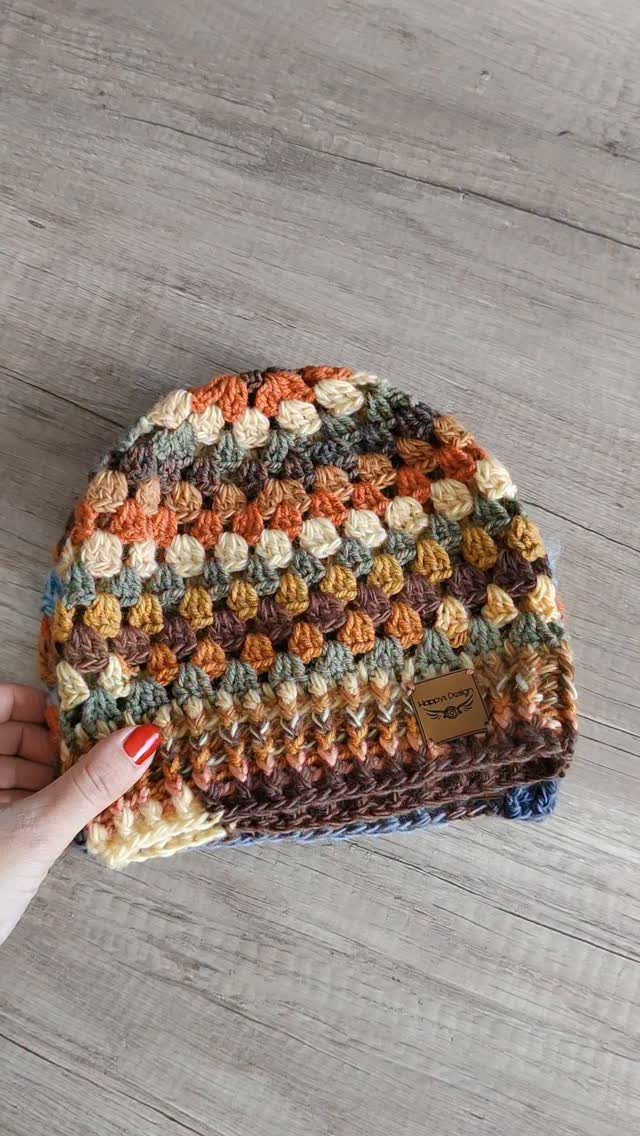 Multi-colored crochet beanie hat held by a hand over a wooden background