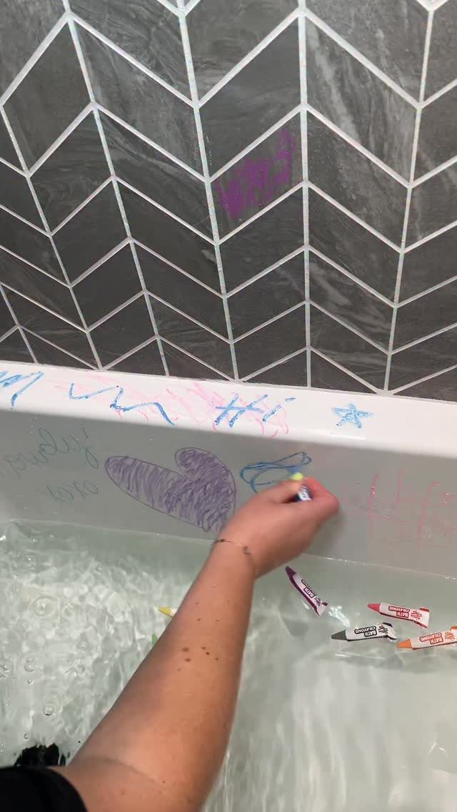 Hand drawing on a white bathtub with colorful bath crayons in soapy water.