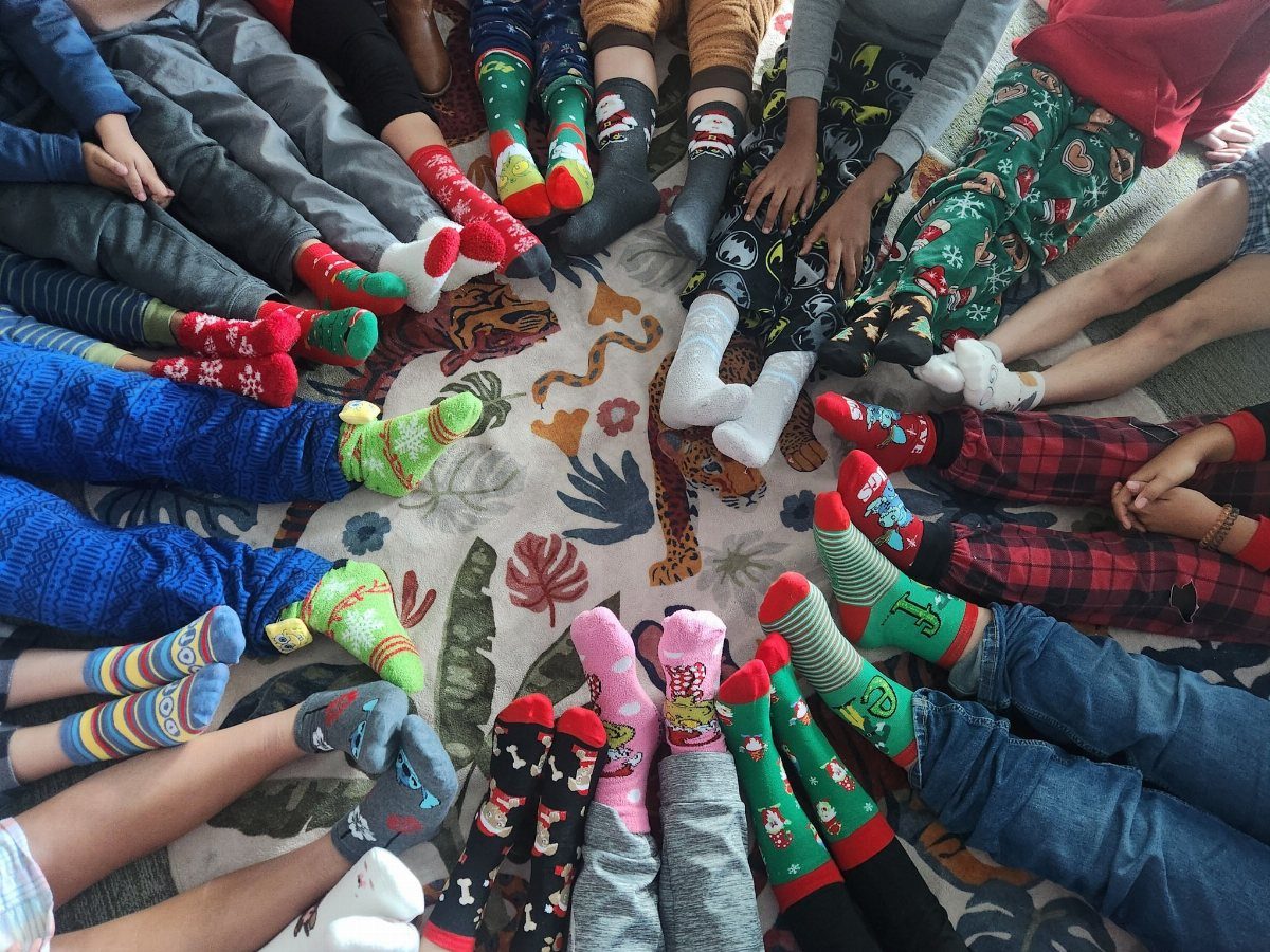 Colorful novelty socks with holiday patterns worn by people sitting in a circle.