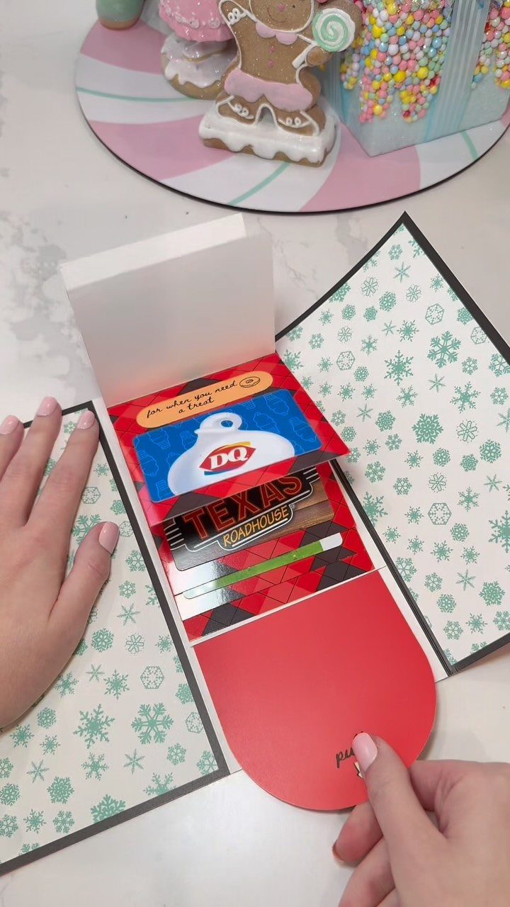 Gift cards inside a red holiday card held by hands on a table