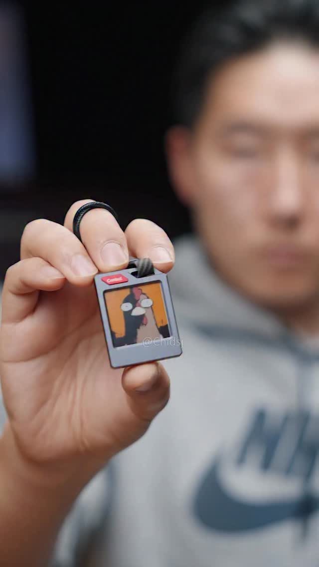 Small polaroid-style keychain held by a hand with a blurred man behind.