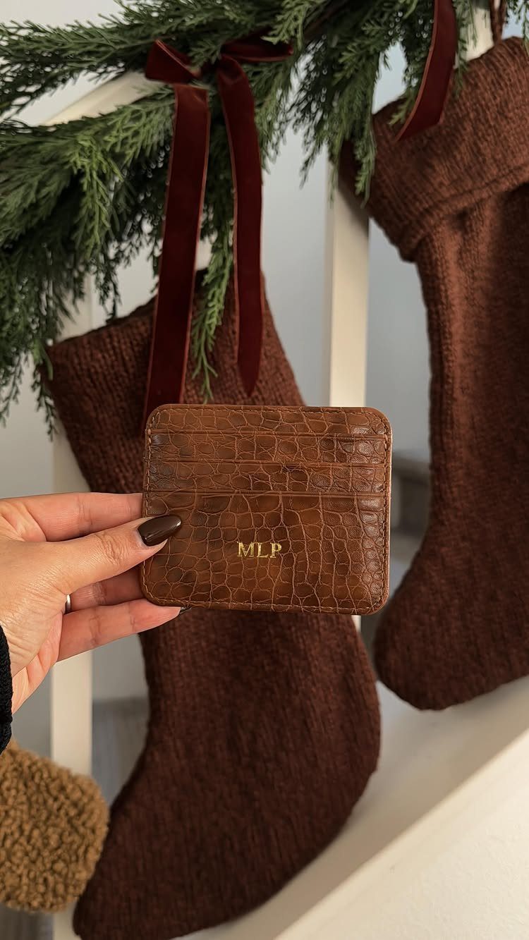 Brown leather card holder held in front of brown knit Christmas stockings