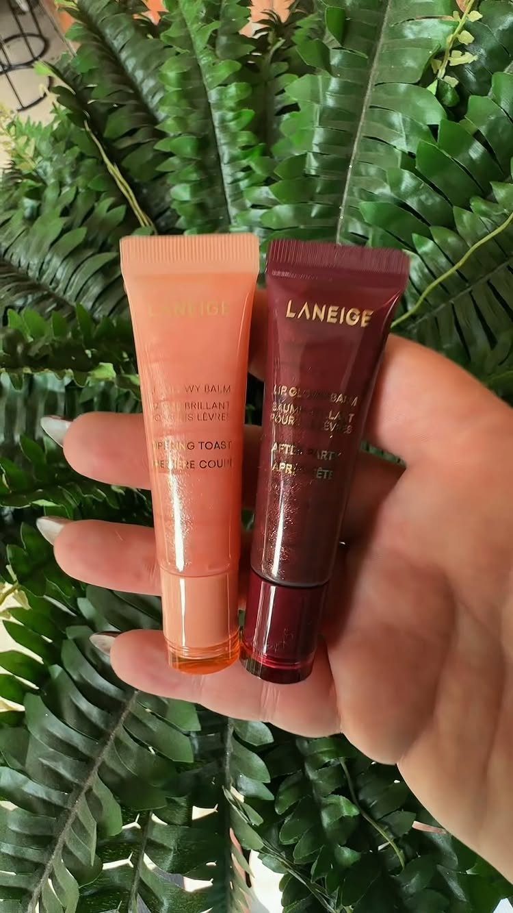 Two small Laneige lip balm tubes held in a hand against green ferns.