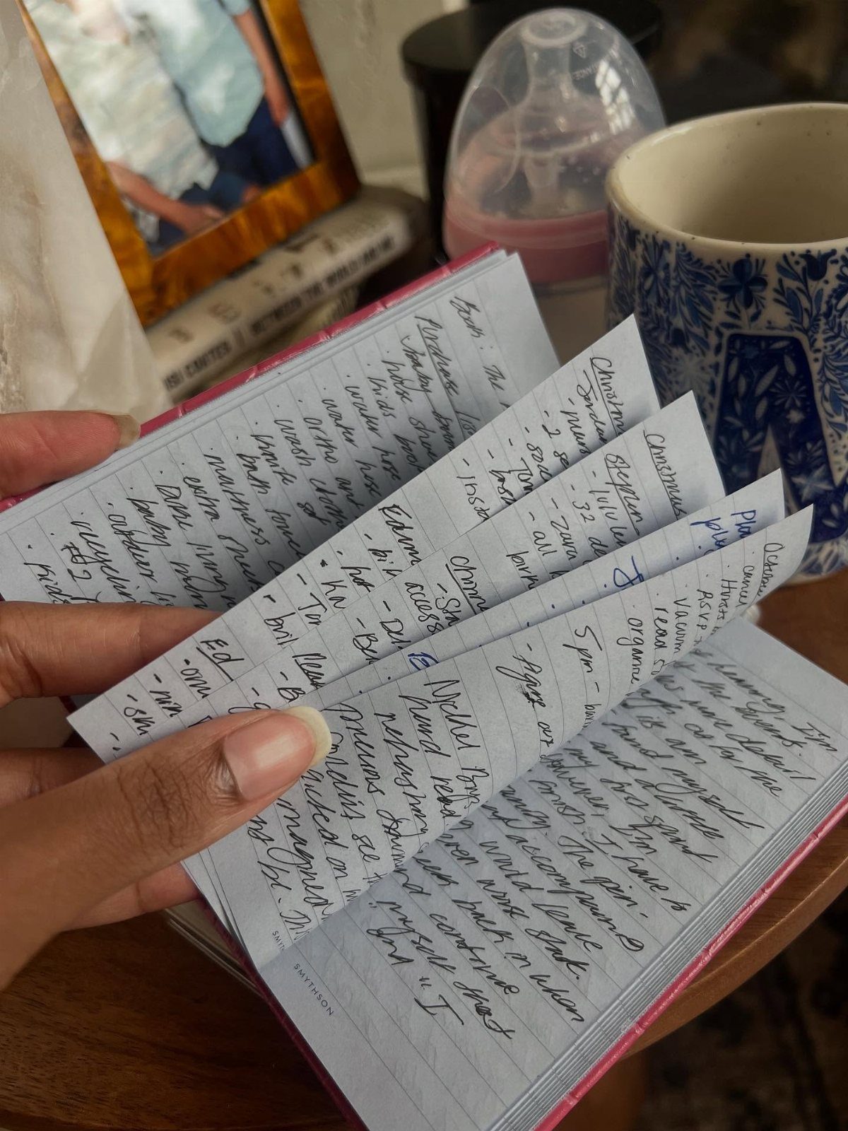 Small pink notebook with handwritten notes held open by a person's hand.