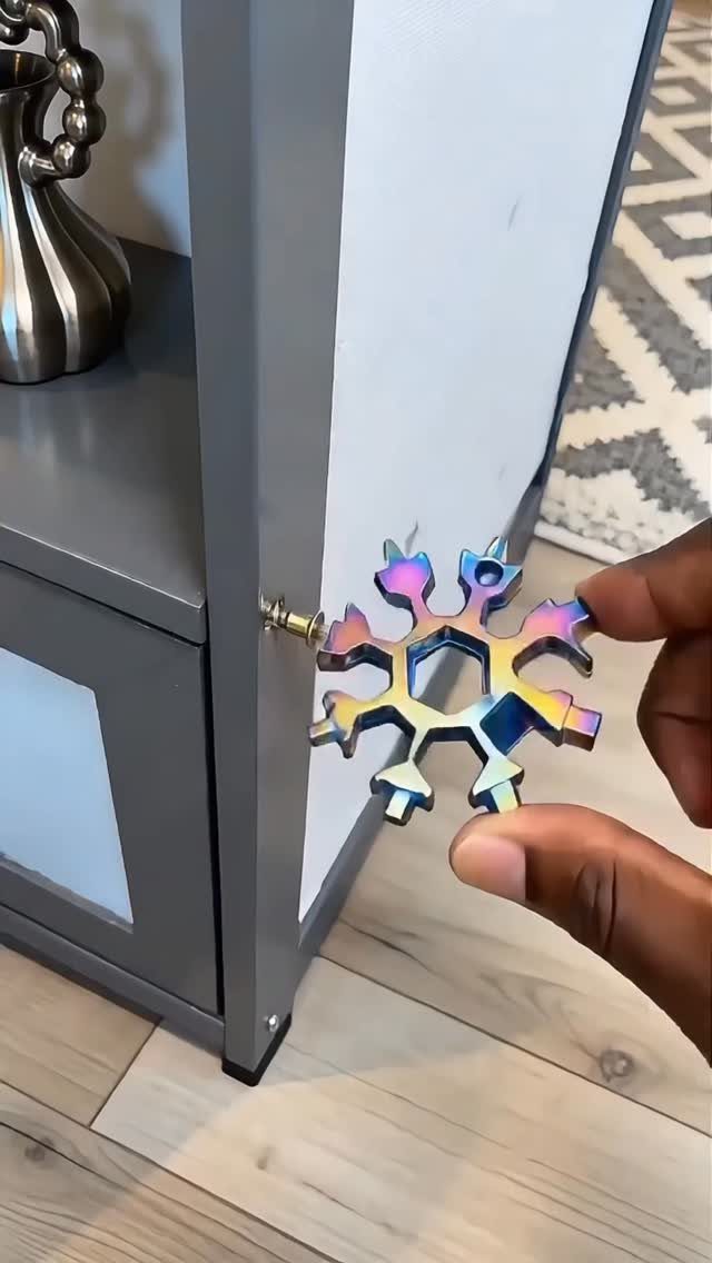 Rainbow metallic snowflake multi-tool held by a hand next to a grey cabinet.