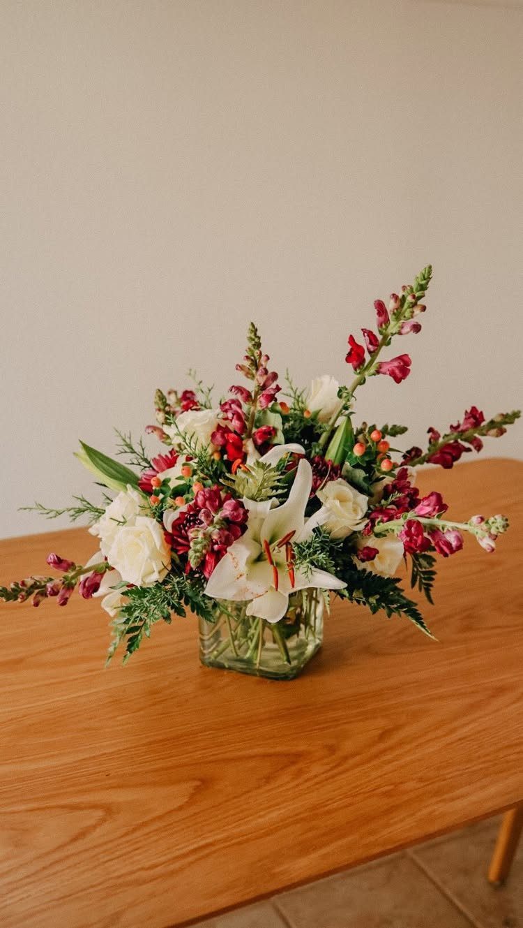 Floral arrangement with white lilies and red flowers in a glass vase on wood.