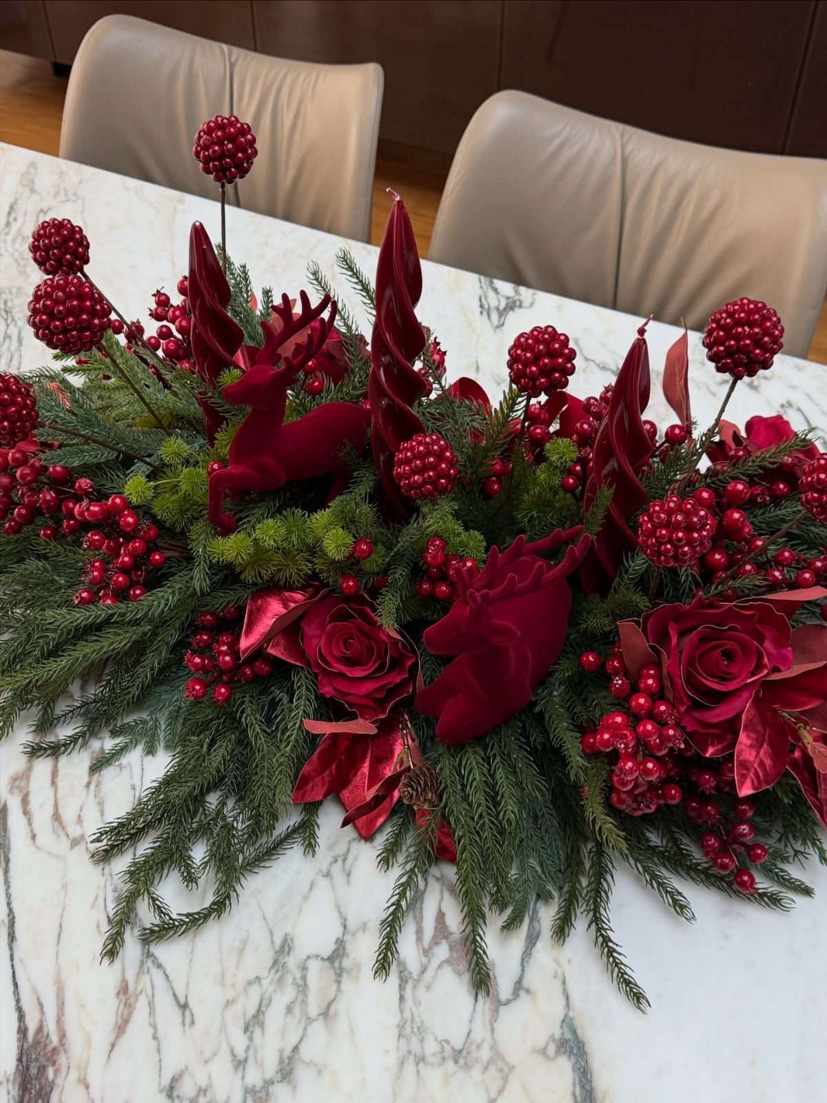 Festive Christmas centerpiece with red roses, berries, and pine needles on marble table