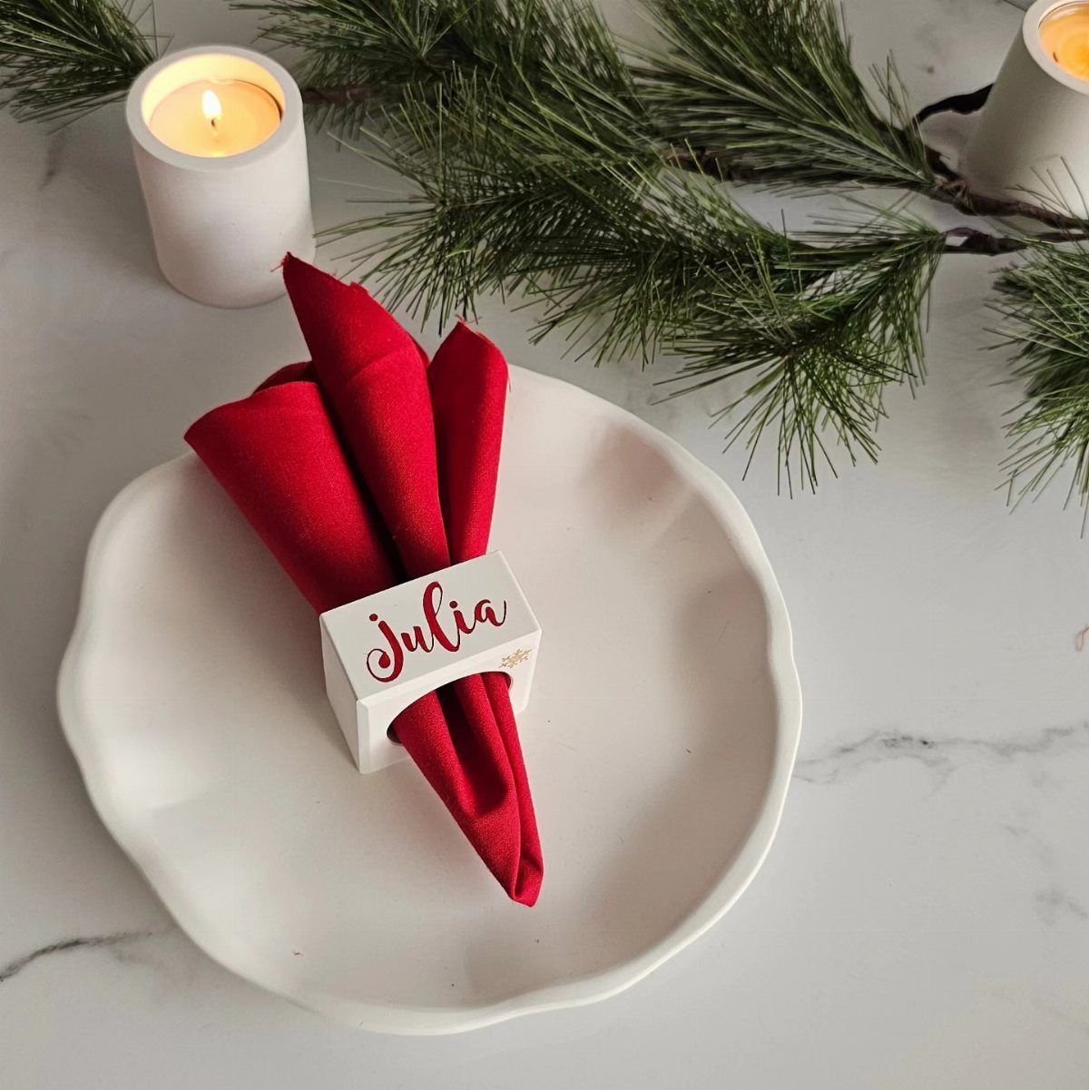Red napkin with a personalized white name ring on a white scalloped plate.