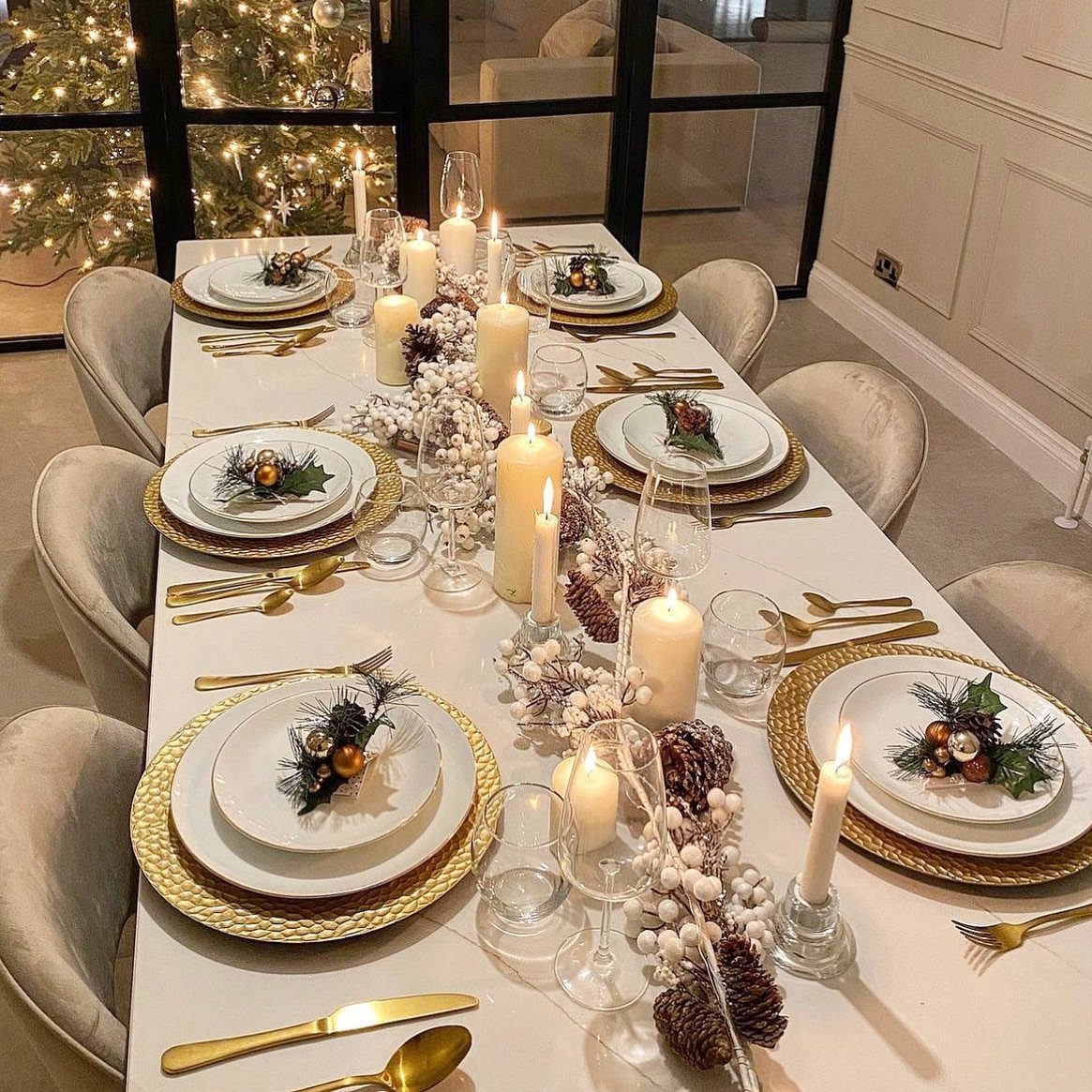 Christmas table setting with gold chargers, white plates, and a festive evergreen centerpiece.