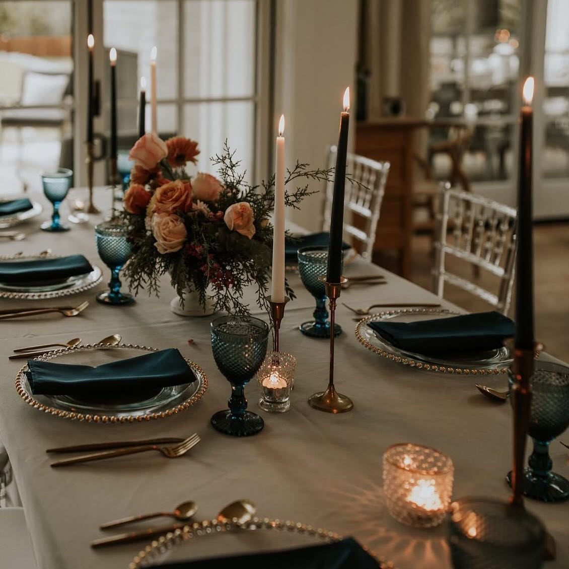 Elegant table setting with gold-rimmed plates, gold cutlery, blue glassware, and floral centerpiece.