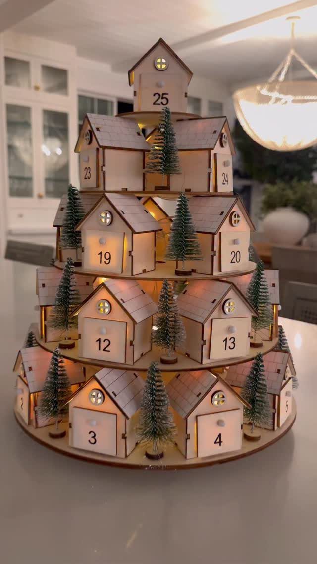 Wooden advent calendar shaped like a tree with numbered houses and miniature evergreens.