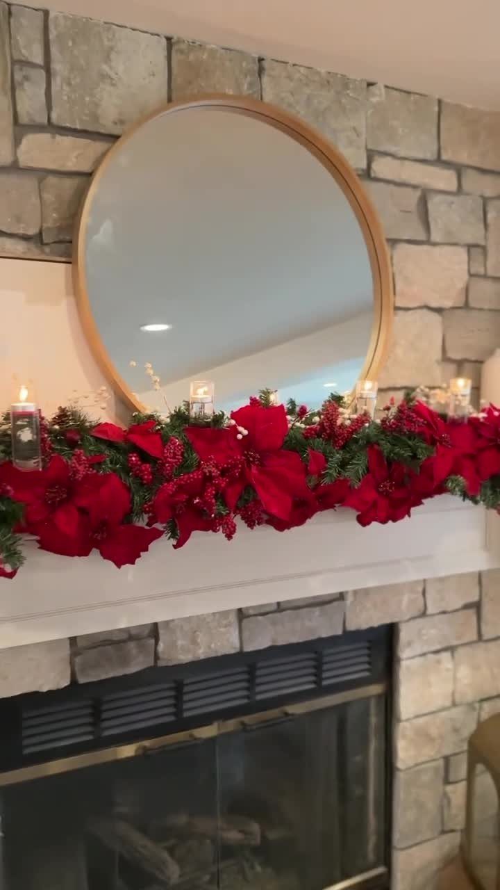 Fireplace mantel decorated with red poinsettias, evergreen greenery, and lit candles.