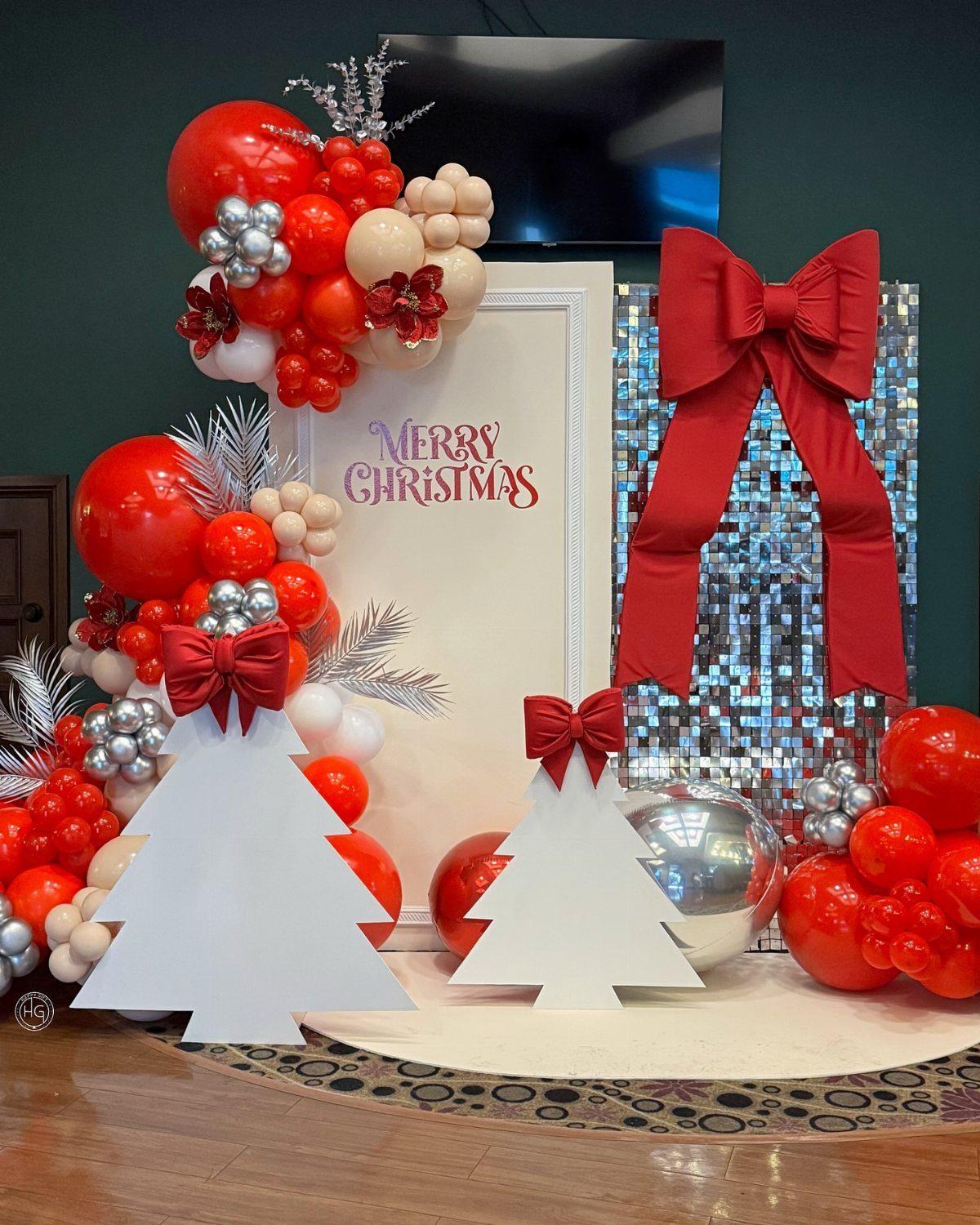 Christmas backdrop with red and silver balloons, white tree cutouts, and red bows.