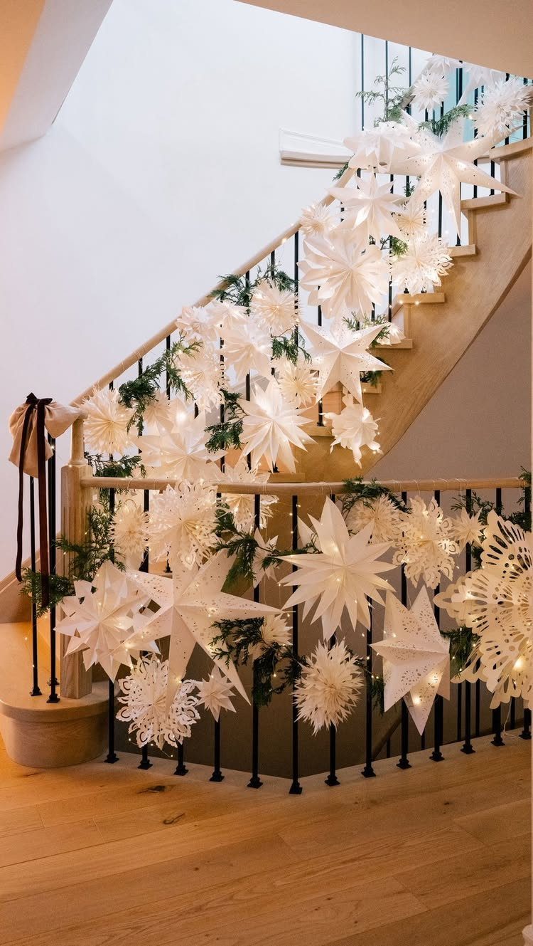 White paper stars and greenery garlands decorating a wooden staircase with fairy lights