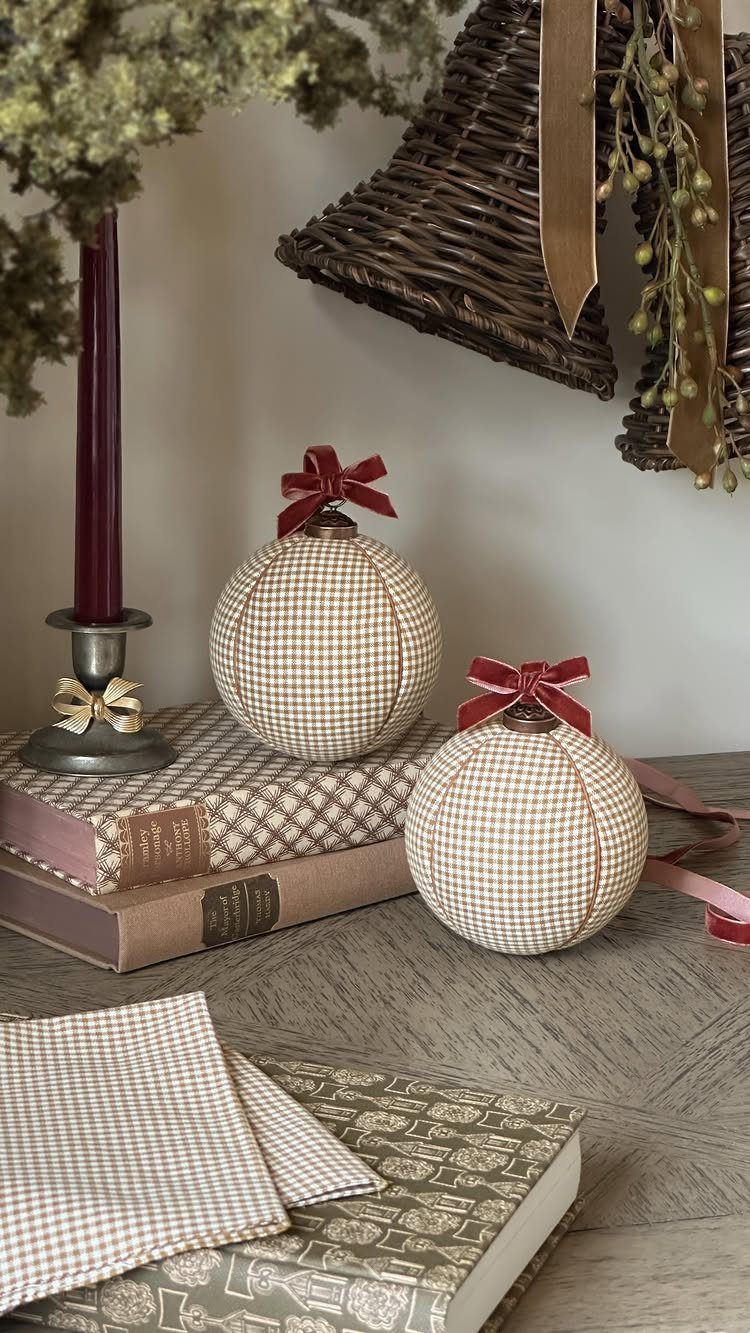 Fabric Christmas baubles with red bows resting on vintage books and a candle.