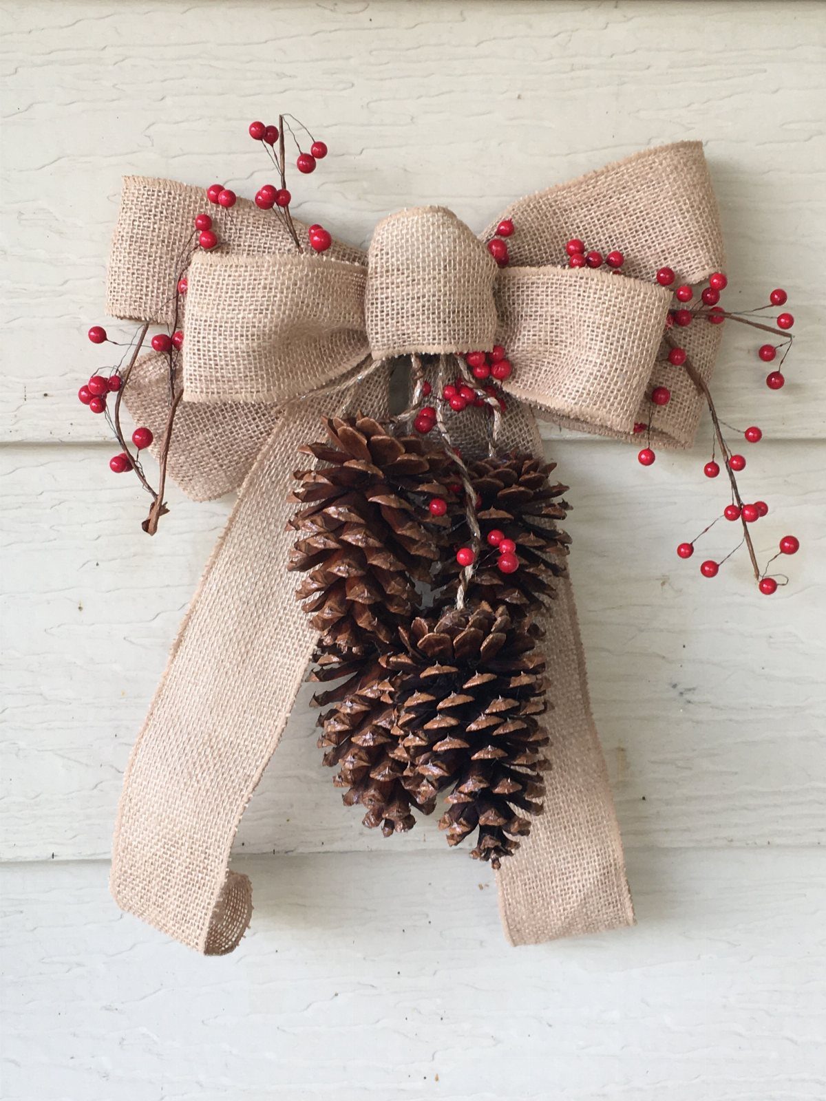 Burlap bow with pinecones and red berries on a white wooden wall