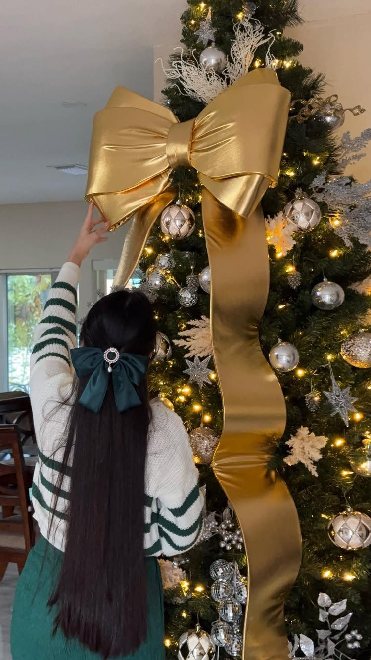 Large gold satin bow on a Christmas tree being adjusted by a woman
